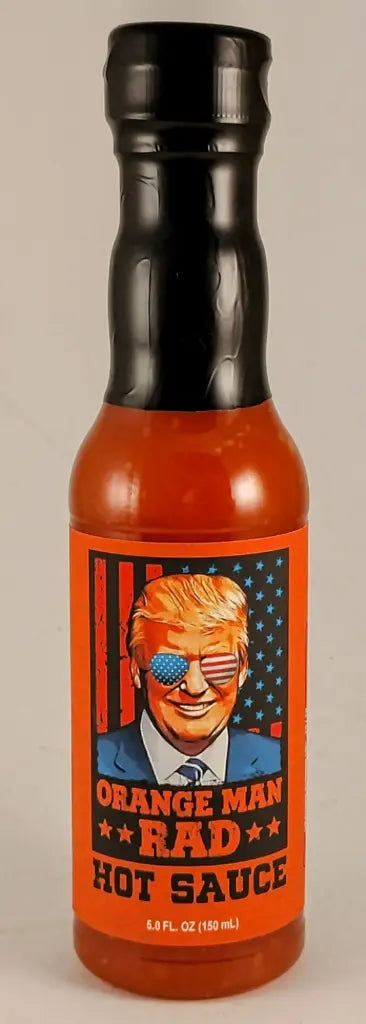 Bottle of “Orange Man RAD Hot Sauce” with a black cap and a bright orange label featuring a stylized illustration of a smiling man in a suit wearing American flag sunglasses, set against a backdrop with stars and stripes. The label text reads “Orange Man RAD Hot Sauce” and the bottle contains red-orange hot sauce. UPC: 188628000647
