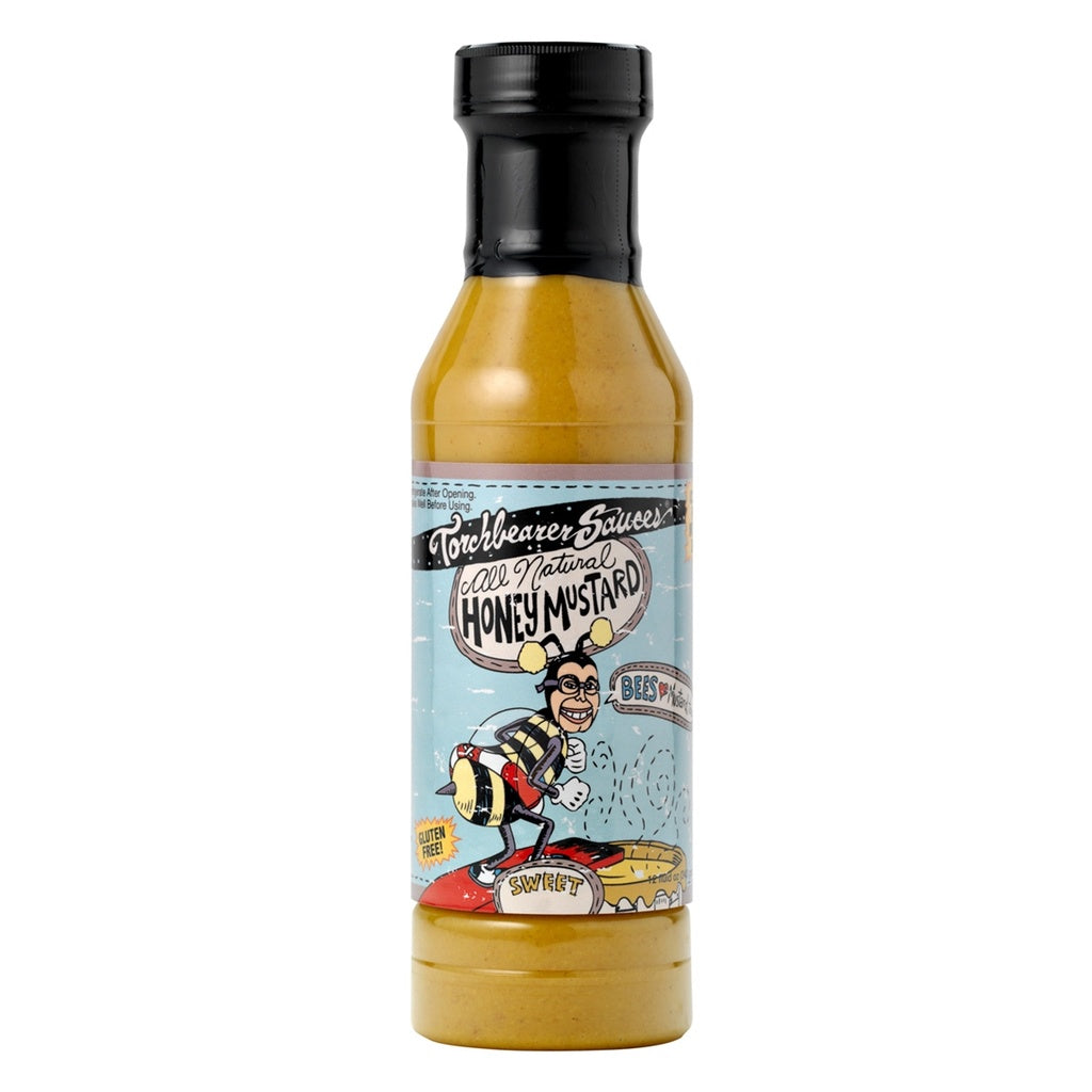 A bottle of Torchbearer Sauces All Natural Honey Mustard, featuring a yellow sauce inside and a black cap. The label has a playful cartoon of a man in a bee costume standing on honeycomb, with light blue background and bold hand-drawn lettering.