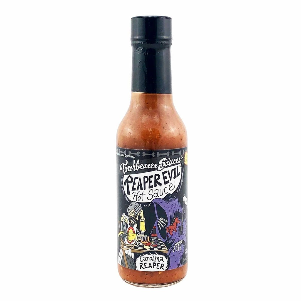 A bottle of Torchbearer Reaper Evil Hot Sauce with a black cap and red-orange speckled sauce inside. The label shows a cartoon reaper and a mad scientist playing a board game, with bold hand-drawn text reading “Reaper Evil Hot Sauce” and “Carolina Reaper.”