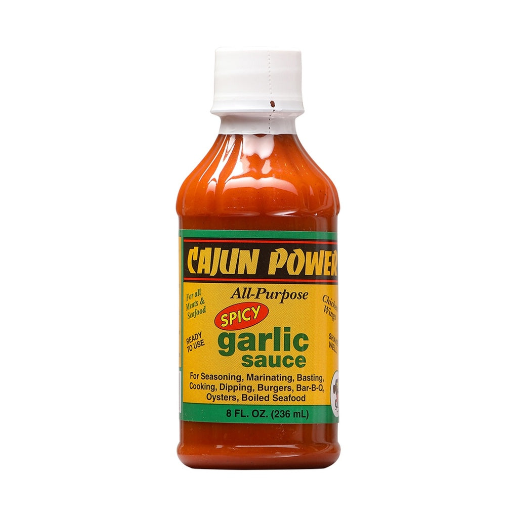 A bottle of Cajun Power Spicy Garlic All-Purpose Sauce. The sauce is bright orange, and the label is yellow with green and black accents. The text highlights “All-Purpose” and “Spicy Garlic Sauce,” noting uses such as seasoning, marinating, basting, cooking, dipping, burgers, BBQ, oysters, and boiled seafood. The bottle contains 8 fl oz (236 ml) and has a white cap.