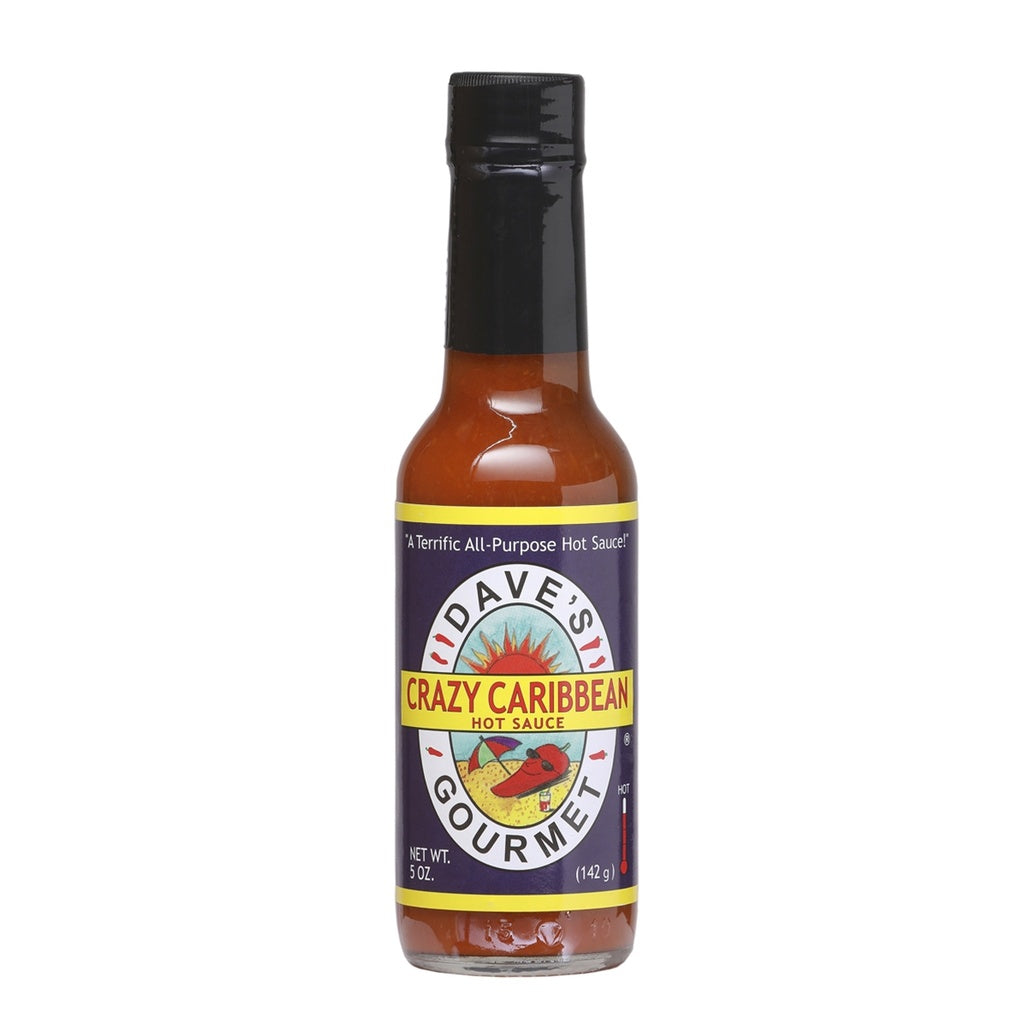Front-facing bottle of Dave’s Gourmet Crazy Caribbean Hot Sauce, showing a purple label with the Dave’s Gourmet sun logo and yellow “Crazy Caribbean Hot Sauce” banner, on a 5 oz glass bottle with black cap, NET WT. 5 oz (142 g) displayed at the bottom; UPC 753469000561.
