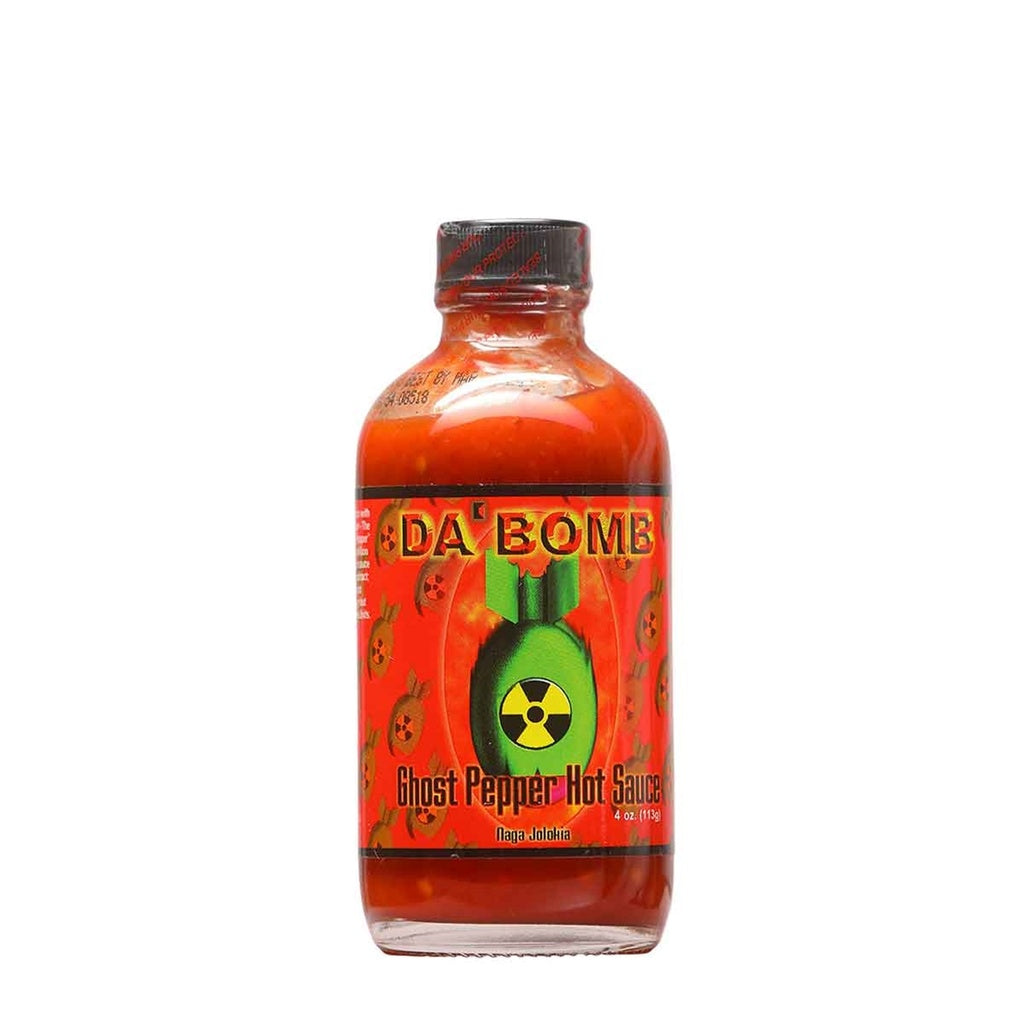 A 4-ounce bottle of Da’ Bomb Ghost Pepper Hot Sauce. The bottle is filled with bright red sauce and has a black cap. The label is red with small bomb icons and features a large green bomb graphic with a radiation symbol, along with the text “Da’ Bomb Ghost Pepper Hot Sauce – Naga Jolokia.”