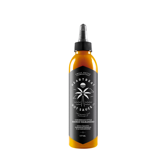 Tall squeeze bottle of Heartbeat Caribbean Style Mango Habanero Hot Sauce with black label, palm tree graphic, and golden mango-colored sauce; labeled 177 mL / 6 fl oz.