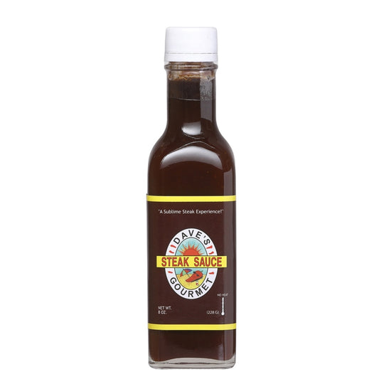 A rectangular 8-oz glass bottle of Dave’s Gourmet Steak Sauce filled with dark brown sauce. The label is deep brown with yellow borders and features the Dave’s Gourmet logo with “STEAK SAUCE” in red text. The bottle has a white cap and shows “NET WT. 8 OZ (228 g)” near the bottom. UPC: 753469000684
