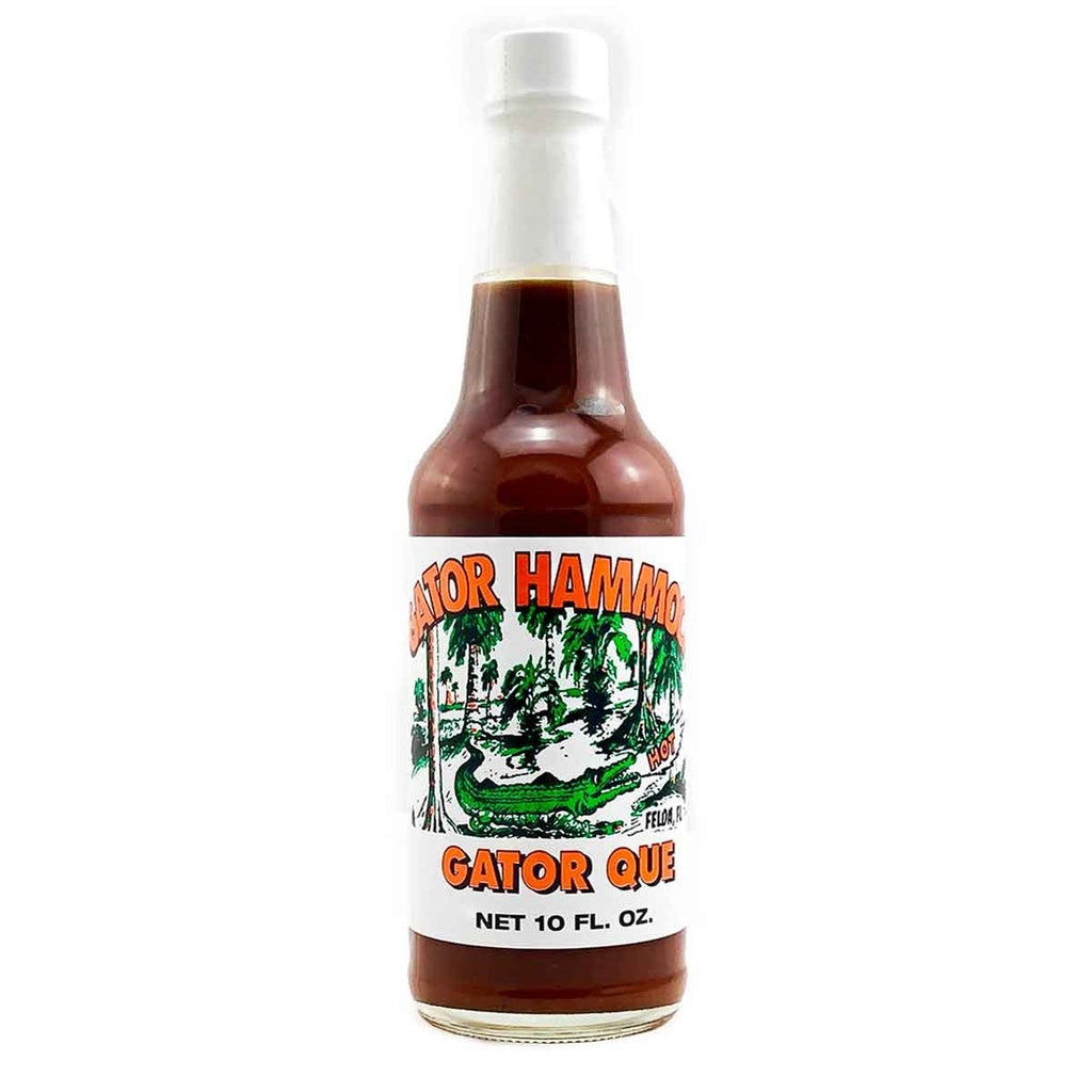 A glass bottle of Gator Hammock Gator Que Barbecue Sauce with a white label featuring an illustrated alligator in a swamp scene and the text “Gator Que,” net 10 fl oz. UPC 748309000894.