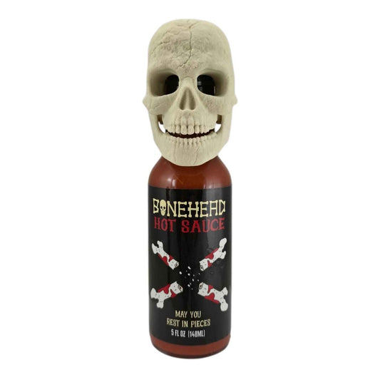 A 5-fl-oz bottle of Bone Head Hot Sauce with a black label featuring bone graphics and red lettering. The bottle is topped with a detailed 3D-printed beige skull with an articulated jaw. The label reads “Bone Head Hot Sauce – May You Rest in Pieces.” UPC 701705500344.
