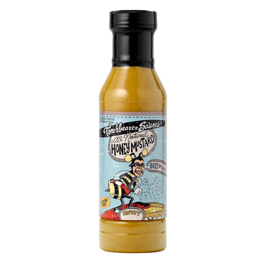 A bottle of Torchbearer Sauces All Natural Honey Mustard, featuring a yellow sauce inside and a black cap. The label has a playful cartoon of a man in a bee costume standing on honeycomb, with light blue background and bold hand-drawn lettering.