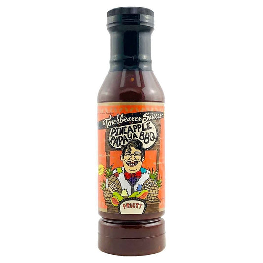 A bottle of Torchbearer Pineapple Papaya BBQ Sauce with a black cap and dark reddish-brown sauce inside. The label features a vibrant cartoon of a smiling man holding pineapples and papayas, with bold text reading “Pineapple Papaya BBQ” and “Fruity.”