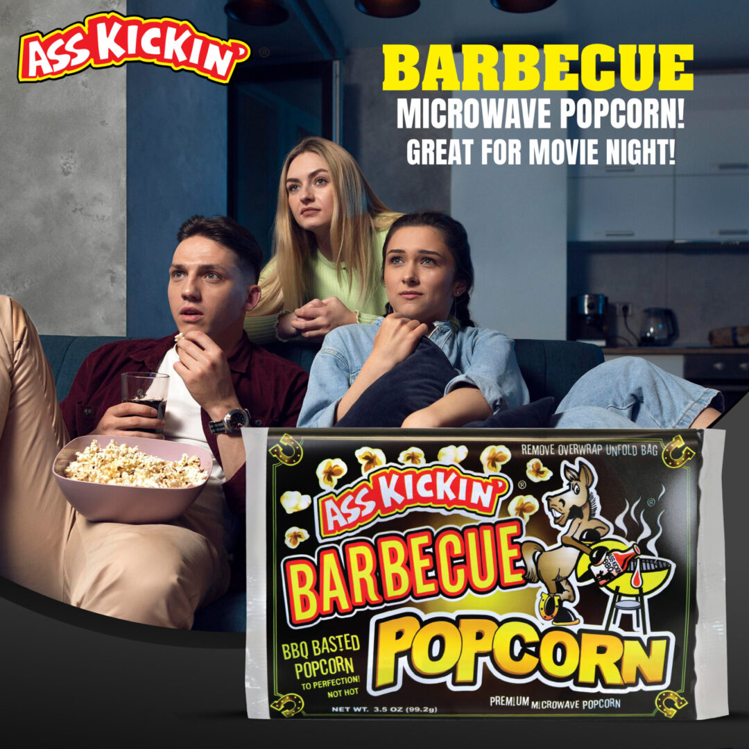 Ass Kickin Barbecue Popcorn package shown in front of a lifestyle scene of three people watching popcorn on a couch, with promotional text reading 'Barbecue Microwave Popcorn! Great for Movie Night!'.