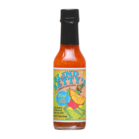 A bottle of Blind Betty's Blind in the Rind Hot Sauce with a vibrant label featuring citrus fruits and fiery pepper imagery. The background suggests a tropical Caribbean beach scene with sun, palm trees, and a feeling of warmth and flavor adventure. UPC: 830139000035.