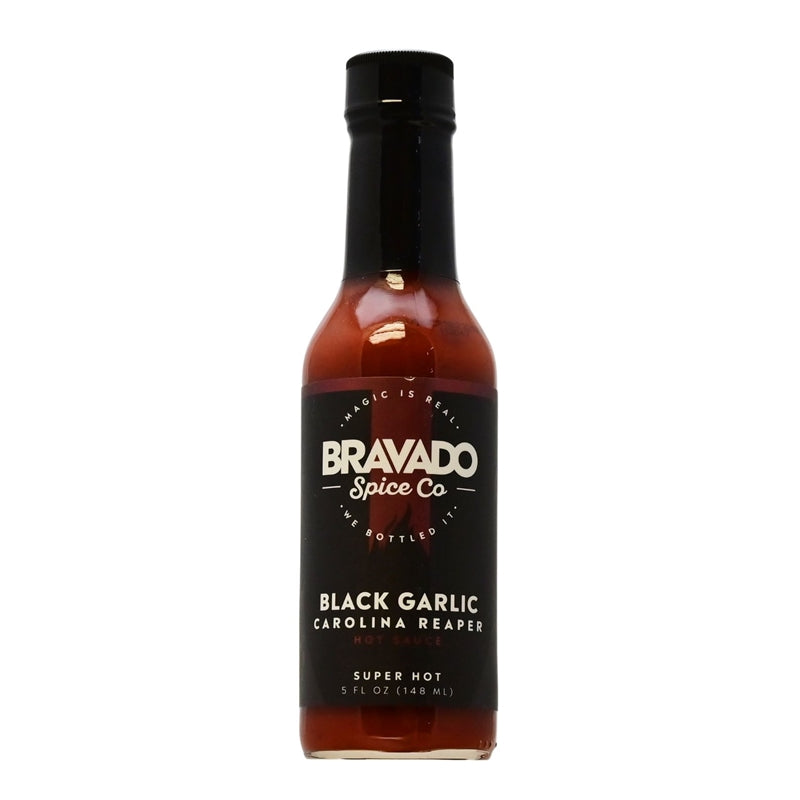 A bottle of Bravado Spice Co. Black Garlic Carolina Reaper Hot Sauce, featuring a dark and bold label design. The sauce's name is displayed prominently. The description emphasizes the combination of Carolina Reaper pepper and black garlic, highlighting the fiery heat and intense flavor. The ingredients, heat level, UPC code 850771005168, and nutrition facts are mentioned.