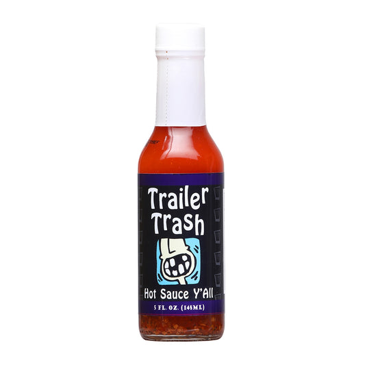 A bottle of Trailer Trash Cayenne Pepper Hot Sauce, featuring a vibrant label with a trailer park theme, including a toothless trailer home owner with the words, Hot Sauce Y'all at the bottom. The 5 oz. bottle contains a blend of cayenne peppers, distilled vinegar, salt, black pepper, natural gum, butter flavor, and citric acid. UPC: 095488103459.